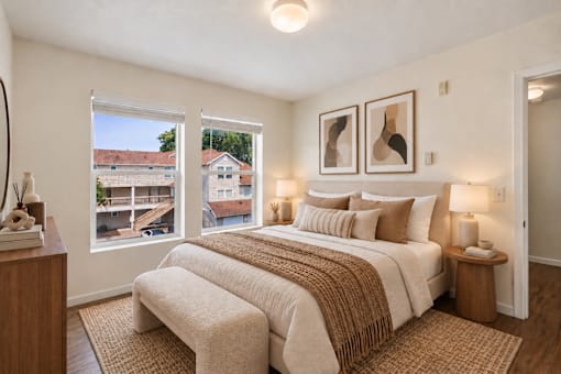 A bedroom with a large bed and a view of a residential area outside the window.