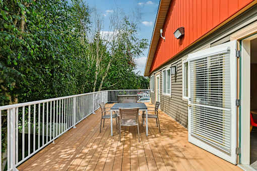 A wooden deck with a table and chairs is surrounded by greenery.