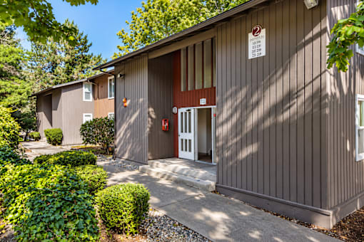 A building with a brown facade and a red door is surrounded by green bushes.
