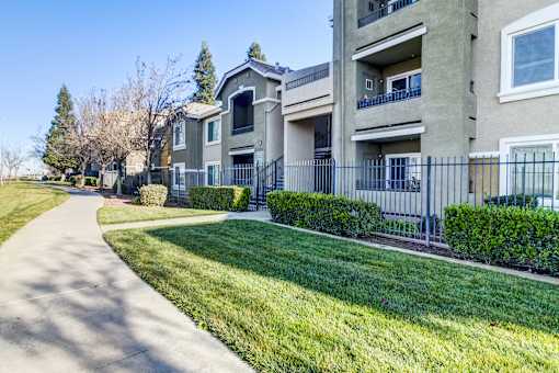 A residential building with a well-maintained lawn and a sidewalk at AGAVE APARTMENTS, Elk Grove, CA