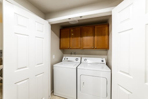 an empty laundry room with white appliances and wooden cabinets
