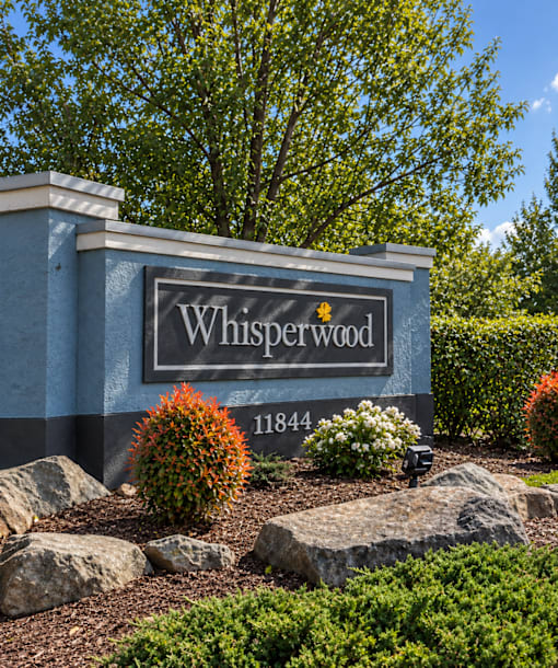 A sign that says Whisperwood in front of some trees.