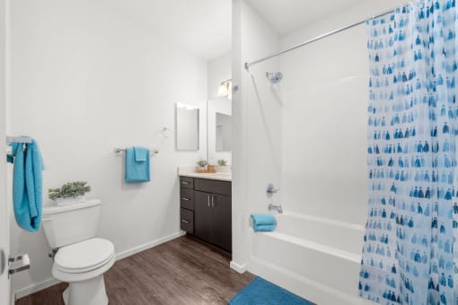 Olympia Apartments - Briggs Village - Bathroom Area with Blue Shower Curtains, Dark-Wooden Vanity, and White Walla