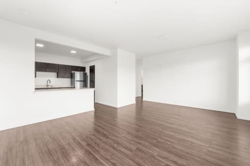 an empty living room with a kitchen in the background