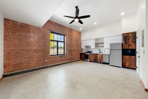 an empty living room with a brick wall and a ceiling fan