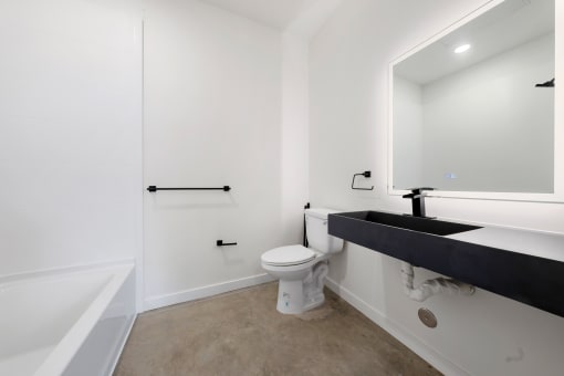 Pet-Friendly Apartments in Upper Land Park Sacramento CA - Market Club at The Mill - Plain Bathroom with Concrete Floor, White Walls, Toilet, Black Hardware and Sinktop Shower, and Tub