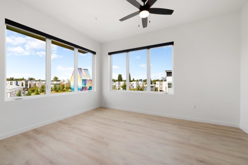 an empty living room with large windows and a ceiling fan