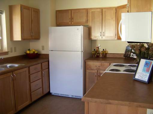 A white refrigerator in a kitchen with wooden cabinets.at Bridge Meadows North Portland 55+, Portland, 97203