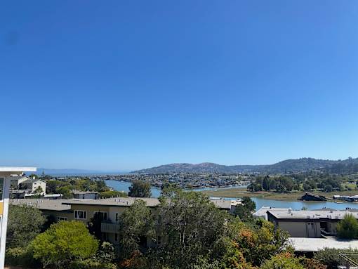 A view of a residential area with houses and trees in the foreground and a body of water and mountains in the distance.at Via Casitas, Greenbrae