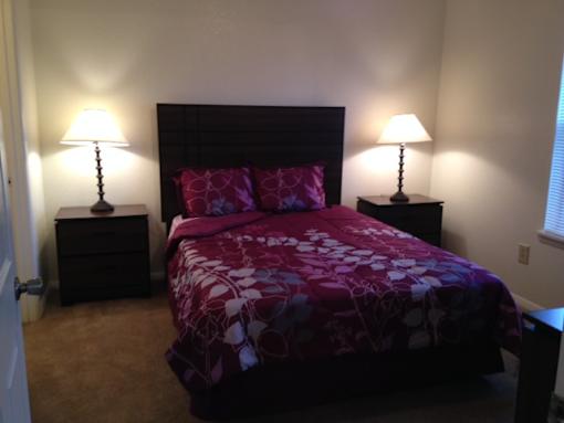 A bed with a purple comforter and two matching lamps.