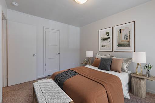 A bedroom with a bed, two lamps, and two framed pictures on the wall at Lake Washington Apartments, 98118