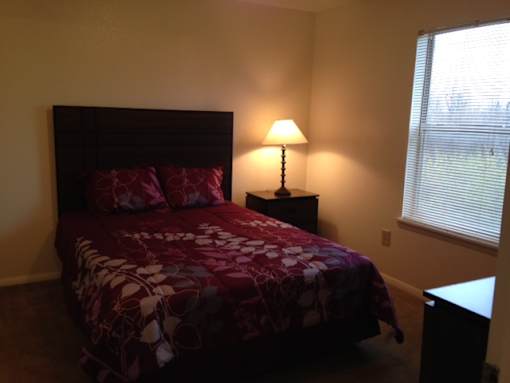 A bed with a red and white comforter sits in a room with a lamp on a side table.