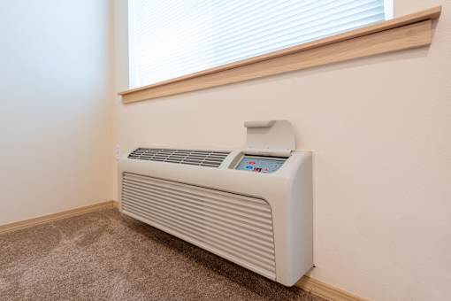 A white electric heater is on the floor next to a window. at Fairview Village Apartments, Fairview, 97024