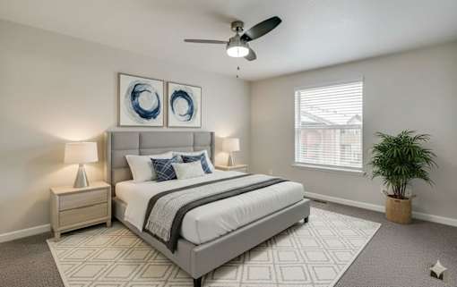 A bedroom with a large bed, a ceiling fan, and a potted plant.