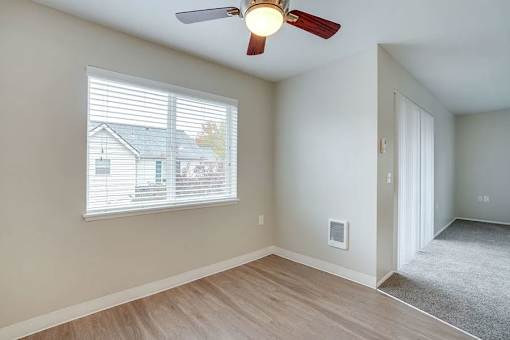 A room with a ceiling fan and a window overlooking a house.