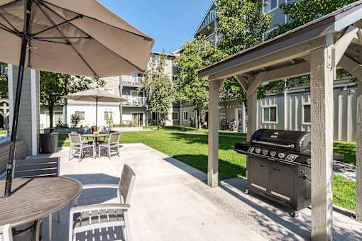 A patio with a grill and chairs under an umbrella.