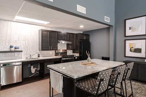 A kitchen with a table and chairs in the foreground and a countertop with a sink and a dishwasher.
