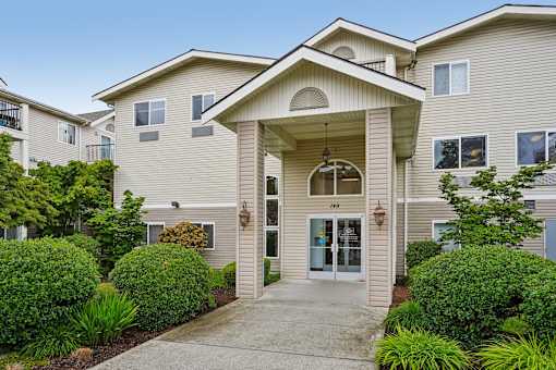 A beige building with a front entrance and bushes at Vintage at Burien,Burien,98168