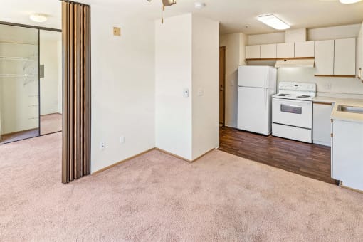 an empty living room with a kitchen with white appliances