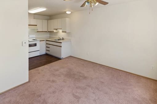 an empty living room and kitchen with white appliances and carpeting