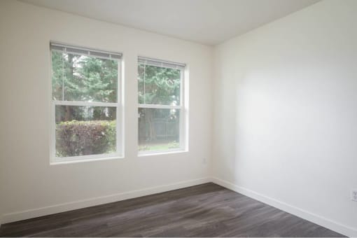 an empty room with two windows and a wood floor at Quail Run Apartments, WA
