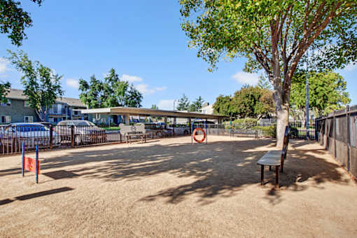 A playground with a red and white sign, a bench, and a tree at The Henley Apartments, Suisun City, 94585