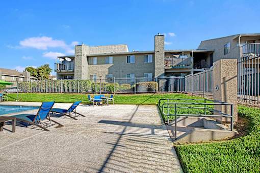 A sunny day at a poolside with chairs and a building in the background at The Henley Apartments, California