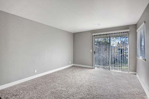 A room with a carpeted floor and a window with a metal gate at The Henley Apartments, Suisun City, CA