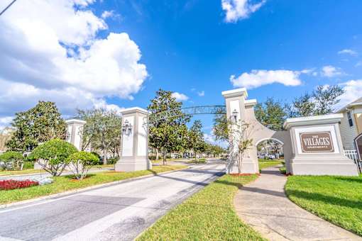 The entrance to a place called Villages is shown with a clear blue sky above at The Villages on Millenia Apartments, Orlando, FL