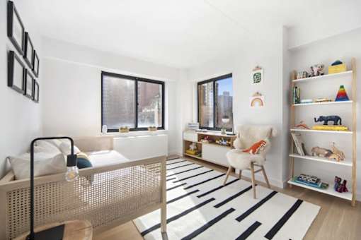 A white bedroom with a bed, chair, and shelves.