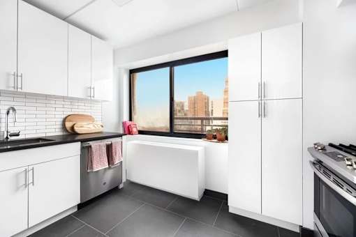A modern kitchen with white cabinets and a view of the city.