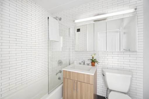 A white tiled bathroom with a wooden vanity and a white toilet.