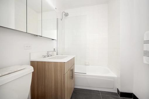 A white bathroom with a wooden cabinet and a white tub.