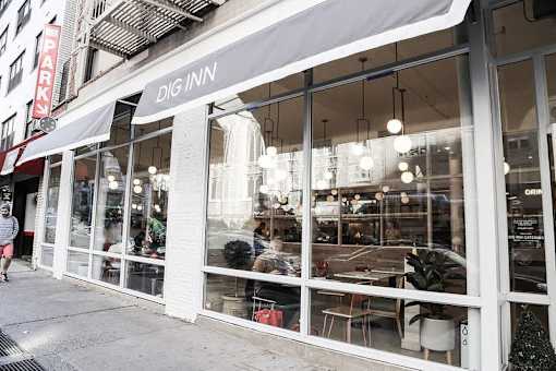 A white building with a black awning that says "Dig Inn".