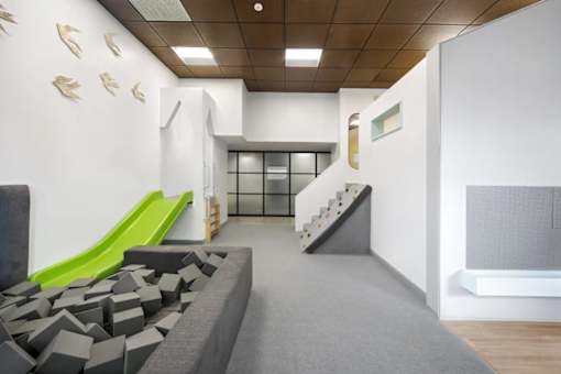 A room with a green slide and grey couch.