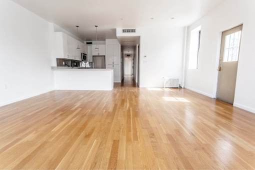 A spacious room with wooden flooring and white walls.