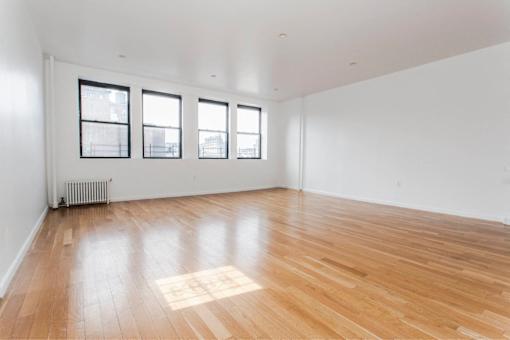 A room with wooden flooring and three windows.