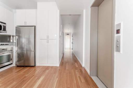 A long hallway with a white wall and a white door.