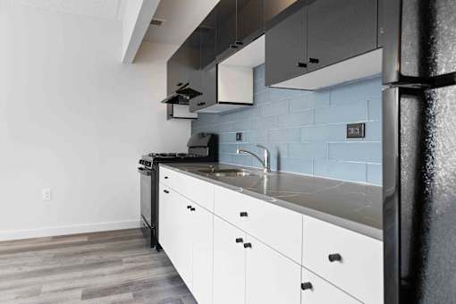 A kitchen with white cabinets and a black refrigerator.