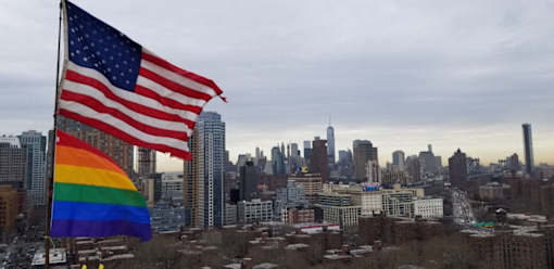 A rainbow flag is displayed next to an American flag in a city.