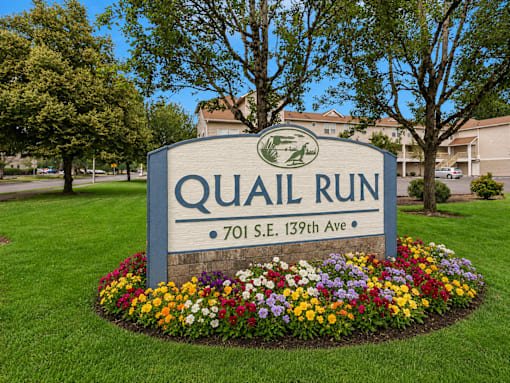 A sign for Quail Run is surrounded by flowers.