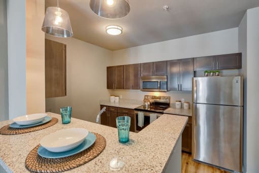 Airway Heights Apartments - Salish Flats - Kitchen with Bar Countertop, Wooden Cabinets, and Stainless-Steel Appliances at Salish Flats APARTMENTS, Airway Heights, WA