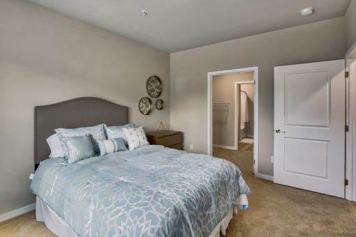 Two-Bedroom Apartments in Airway Heights, WA - Salish Flats - Bedroom with Blue Comforter Set, Wooden Nightstand, and Entrance to Spacious Closet at Salish Flats APARTMENTS, Airway Heights