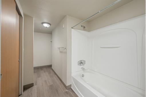 A white bathtub is in a small bathroom with wood flooring at VISTA CREEK Apartments, Laughlin, NV 