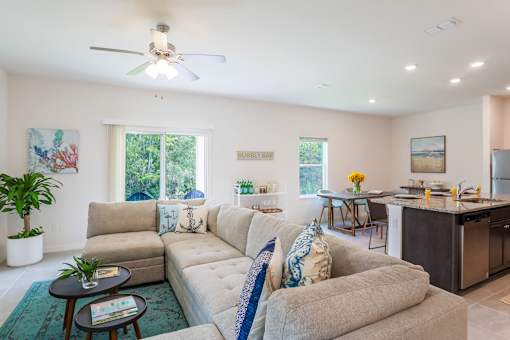 A living room with a beige couch and a ceiling fan.