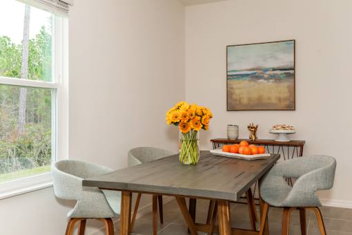 A dining table with chairs and a vase of flowers in the middle.