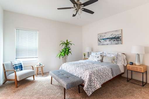 A bedroom with a bed, chair, and potted plant.