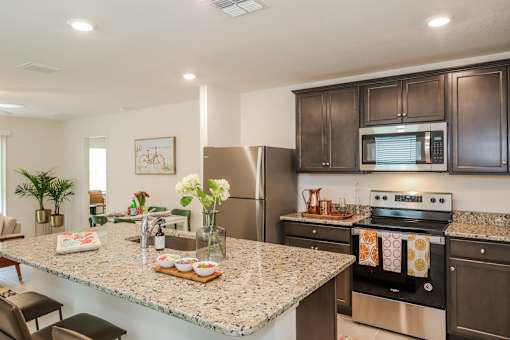 A modern kitchen with dark wood cabinets, granite countertops, stainless steel appliances, and a cozy dining area in the background.