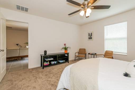 A bedroom with a large bed, a ceiling fan, and a chair.