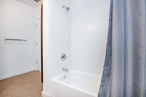 A white bathroom with a white tub and a blue shower curtain.